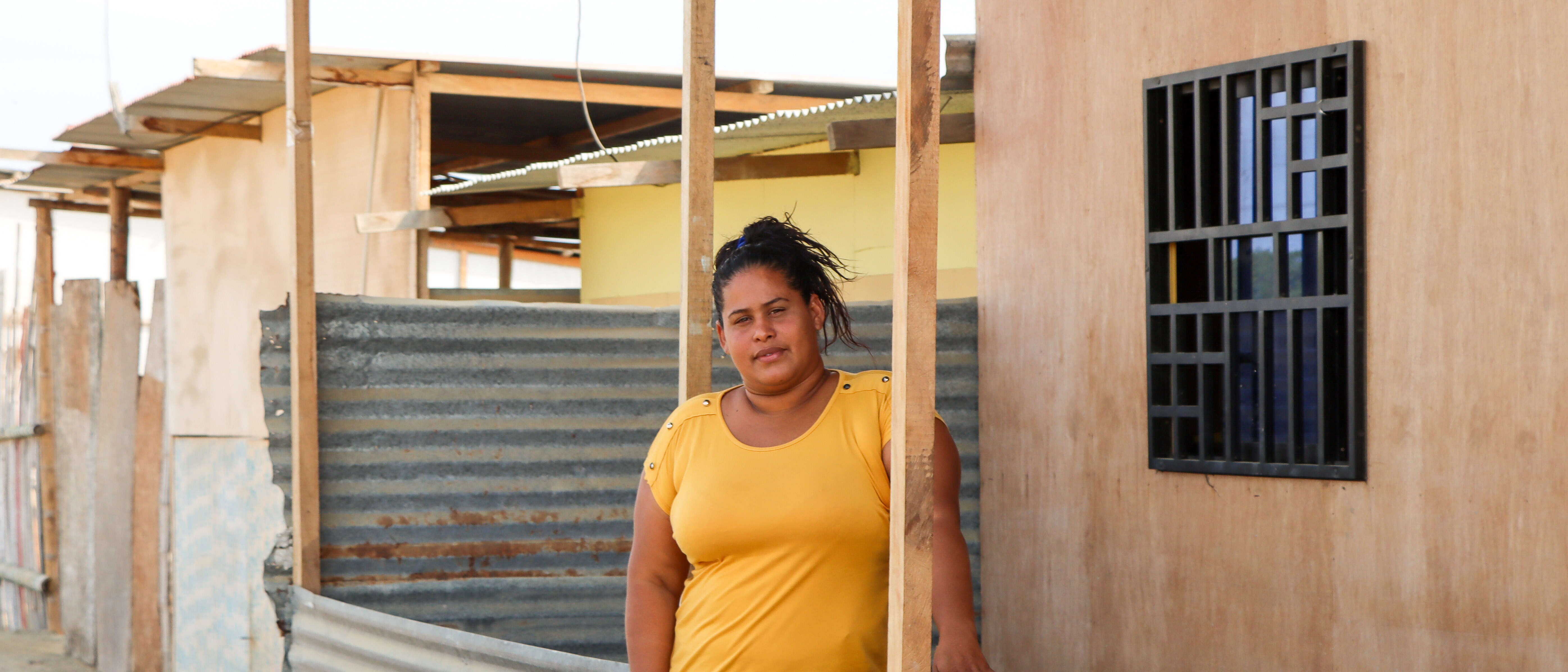 A woman stands outside a makeshift shelter and poses for a photo.