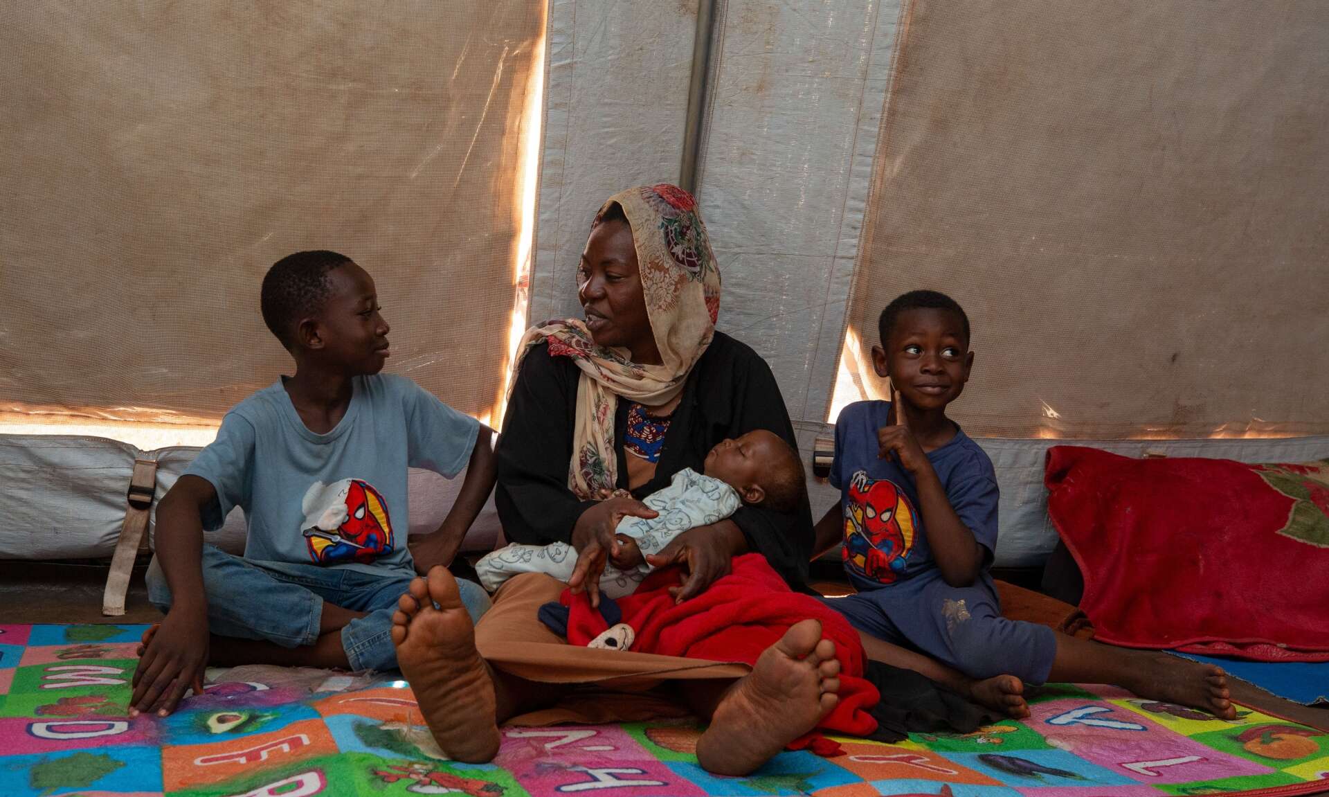 A family sits together on the floor of a makeshift shelter in a camp for displaced people.