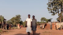 Two girls pose for a picture in South Sudan. They are both smiling.