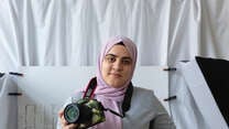 Hamida smiles, holding her camera in her hand.