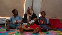 A family sits together on the floor of a makeshift shelter in a camp for displaced people.